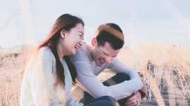  Een foto van een Aziatische vrouw en een westerse man die hartelijk lachen terwijl ze naast elkaar in een grasveld zitten