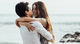 Een foto van een man die een vrouw in zijn armen draagt ​​langs de kustlijn bij een strand